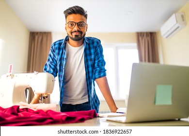 indian tailor asian man designer sewing clothes on sewing machine next to laptop home apartment workplace