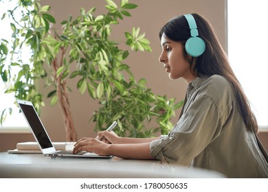 Indian teen girl school college student wear headphones learning watching online webinar class looking at laptop computer elearning lesson making notes or video calling virtual meeting remote teacher.