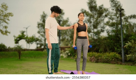 Indian teenager woman standing hold dumbbells do hand lifting muscle workout exercise with young adult gen z professional man gym trainer learning teach healthy body fitness good habit outdoor garden - Powered by Shutterstock