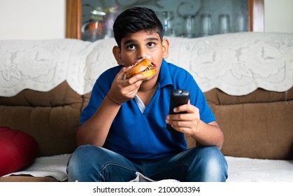 Indian Teenger Kid Watching Tv Or Television By Eating Unhealthy Food At Home - Concept Of Lesieur Activity,time Waste And Unhealthy Lifestyle.