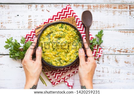 Indian traditional yellow dal food with cilantro in bowl. Woman hands holds Cooked beans. On wooden table white background. Top above view