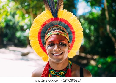 Indian From The Pataxó Tribe With Feather Headdress Looking At The Camera. Indigenous Man From Brazil, With Traditional Face Paintings