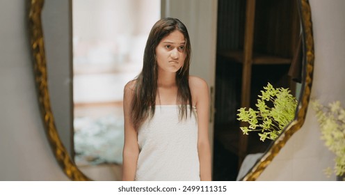 Indian unhappy frustrated young adult gen z beautiful female wrapped white towel on body standing casual look bathroom mirror reflection frizzy long messy hair get ready in morning day - Powered by Shutterstock