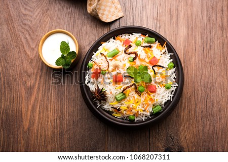 Indian Vegetable Pulav or Biryani made using Basmati Rice, served in a wooden bowl with yogurt. selective focus
