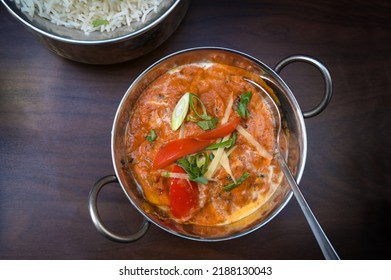 Indian Vegetarian Curry Dish With Tomato And Spring Onions In A Stainless Steel Bowl Served With Rice On A Dark Brown Wooden Table, Copy Space, High Angle View From Above, Selected Focus