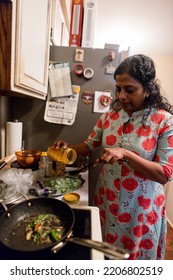 Indian Woman Adding Turmeric To Indian And Peppers In Frying Pan At Home While Cooking With Family