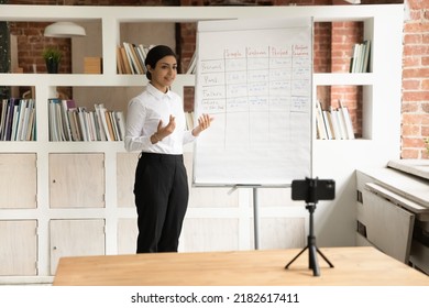 Indian Woman Blogger Standing In Front Of Cell Phone On Tripod Record Educational Webinar English Grammar Class, Explain Tenses Shown On Flip Chart. Improve Language Skill, Tutoring, Education Concept