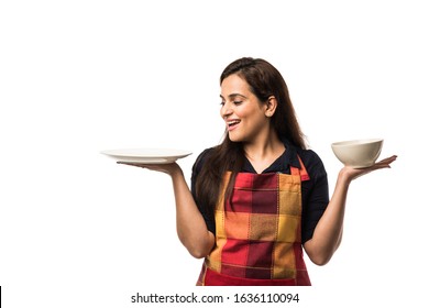 Indian Woman Chef Wearing Apron And Holding Empty Ceramic Dinner Plate And Bowl With Different  Facial Expressions, Standing Isolated Over White Background