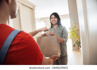 Indian Woman Customer Taking Delivery Paper Eco Bag With Grocery Takeout Food Meal From Man Courier Holding Paper Package Delivering Supermarket Or Restaurant Takeaway Order Standing At Door At Home.