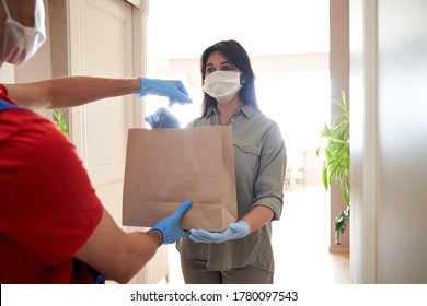 Indian woman customer wearing face mask and gloves taking delivery paper eco bag from man courier holding grocery food package delivering supermarket takeaway order standing at home. Safe delivery.