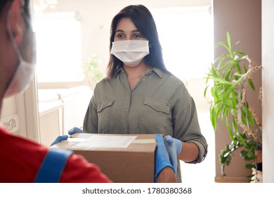 Indian Woman Customer Wears Medical Face Mask Gloves Holds Courier Delivery Box Stands At Home. Deliveryman Or Postman Gives Parcel Package Delivering Post Mail Shipping Order To Indian Female Client.