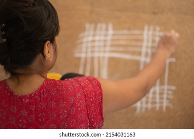 Indian Woman drawing rangoli Kolam on ground - Blurred, selective focus