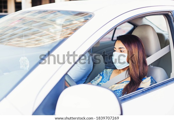 Indian woman driving a car while\
wearing a medical protective face mask for Covid-19\
prevention