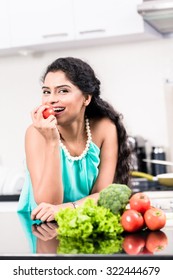 Indian woman eating healthy apple in her kitchen, salad and vegetables on the counter