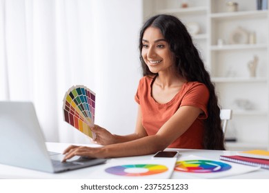 Indian Woman Freelance Graphic Designer Working With Laptop And Color Swatches At Desk In Home Office, Smiling Young Eastern Lady Choosing Color Gamma For New Design Project, Free Space - Powered by Shutterstock