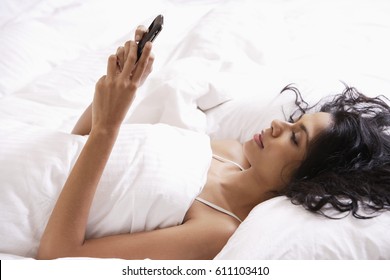 Indian Woman Laying Down In Bed Looking At Phone.