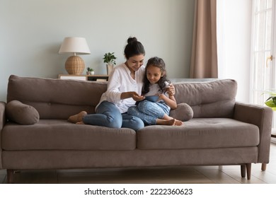 Indian woman and little daughter spend time using digital tablet, sit together on couch at home, buying goods, purchasing toys through retail webstore enjoy new application for fun or kid development - Powered by Shutterstock