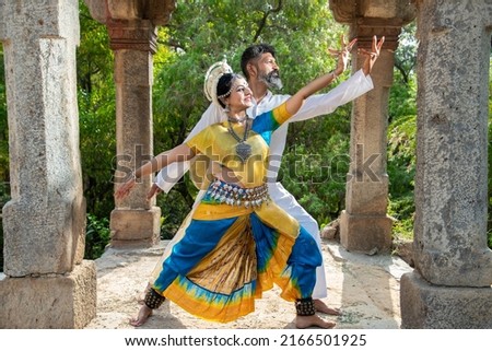 Indian woman Odissi dancer doing classical dance along with teacher or master outdoor. female do Orissi dance training with coach. Traditional  art and culture of india.