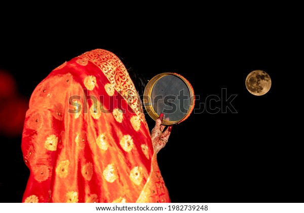 Indian Woman on Left Side\
Standing Back side Doing Karva Chauth Festival at night in front of\
Moon