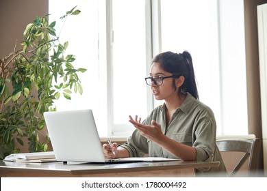 Indian woman online tutor remote teacher wearing glasses speaking to webcam chat explaining online class zoom video call school lesson looking at laptop virtual conference meeting work at home office.