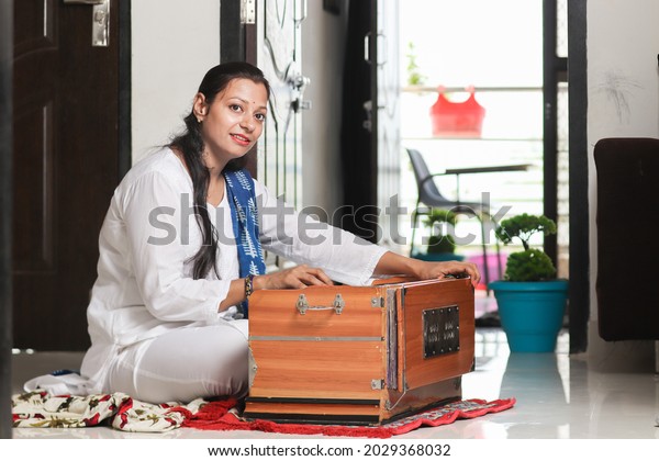 Indian woman\
playing harmonium at home. Female Playing music, She is practicing\
learning cords on  traditional musical instrument.  improving\
creative skills and hobby.\
