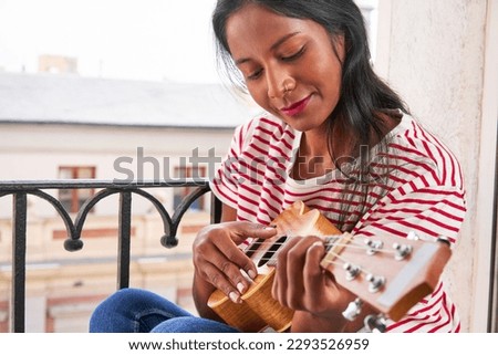 Indian woman playing ukulele on windowsill