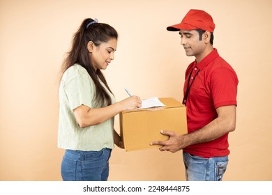 Indian Woman Receiving Box From Courier Man Standing Over Beige Studio Background. Post Package Delivering And Transportation, Couriers Service Concept. Parcel Delivery.Closeup Shot. - Powered by Shutterstock