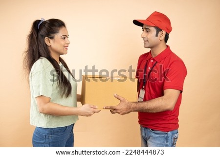 Indian Woman Receiving Box From Courier Man Standing Over Beige Studio Background. Post Package Delivering And Transportation, Couriers Service Concept. Parcel Delivery.Closeup Shot.