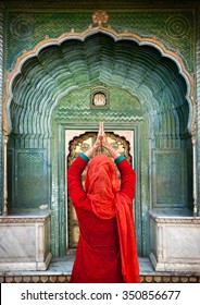 Indian Woman in red scarf with hands in prayer gesture at green gate door in City Palace of Jaipur, Rajasthan, India. Space for your text, can be used as book or magazine cover.