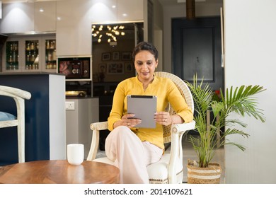 Indian woman sit on chair using tablet gadget at living room