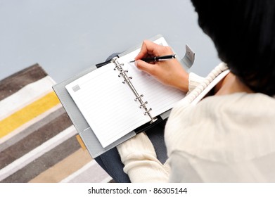 Indian Woman Sits On Her Couch, Writing Into Her Planner