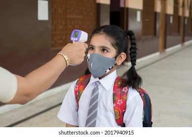 Indian woman teacher using thermometer temperature screening student for fever against the spread of COVID-19 while student coming back to school.