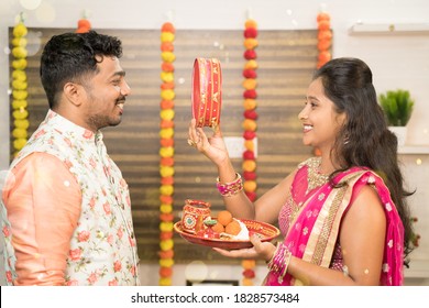 Indian woman in traditional dress seeing her husband or partner through sieve during Hindu Indian religious karwa chauth festival at home