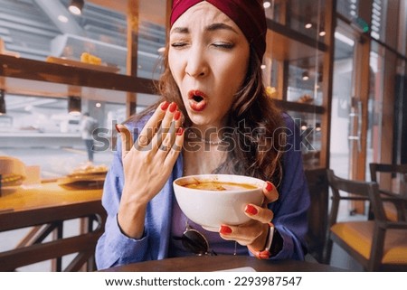 Indian woman tries a spicy and hot Tom Yam soup in a thai cuisine restaurant and reacts funny emotionally. Seasonings and an unhealthy diet with overabundance of pepper