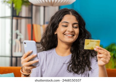 Indian woman use credit bank card and smartphone while transferring money, purchases online shopping cashless order food delivery at home apartment indoors. Happy Arabian girl sitting in room on couch - Powered by Shutterstock