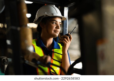 Indian woman worker driving a forklift and using a walkie-talkie at warehouse factory container. communication radio. Inventory and wholesale concept