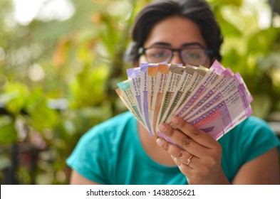 An Indian Women Holding All The Colorful New Released Indian Rupees Currency Notes After Demonetisation In Denominations 10,50,100, 200, 500, 2000 In Her Hands With Her Blur Face In The Background