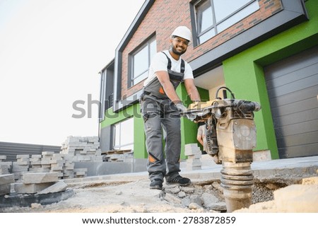 Indian worker using vibratory tamping machine plate compactor on a new patio driveway pavement to apply Polymeric sand to fill joints.