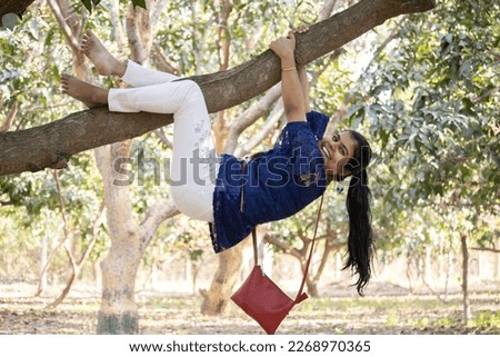 An indian young adult girl playfully climbing a tree in garden