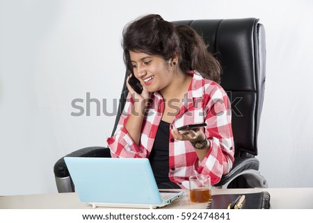 Indian young businesswoman looks busy, working in the office while enjoying a cup of coffee and using a laptop and phone.