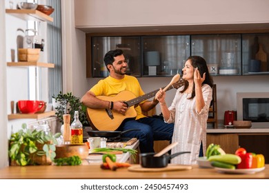 Indian young couple cooking food in kitchen, husband plays guitar and wife sings - Powered by Shutterstock