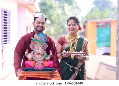 Indian Young Couple Holding Lord Ganesha  On Ganesh Festival While Welcoming Home For Pooja. Couple Wearing Indian Traditional Cloths