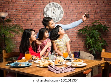 Indian young Family of four eating food at dining table at home or in restaurant. South Asian mother, father and two daughters having meal together - Powered by Shutterstock