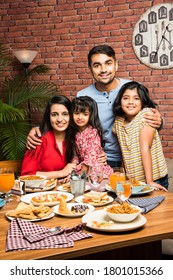 Indian Young Family Of Four Eating Food At Dining Table At Home Or In Restaurant. South Asian Mother, Father And Two Daughters Having Meal Together