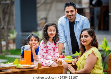 indian young family of four eating meal on dining table in the garden - Powered by Shutterstock