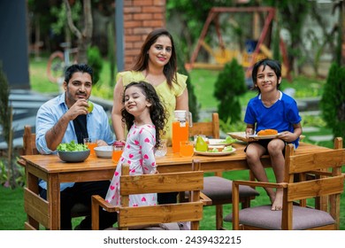 indian young family of four eating meal on dining table in the garden - Powered by Shutterstock