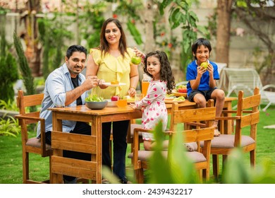 indian young family of four eating meal on dining table in the garden - Powered by Shutterstock