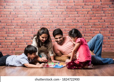 Indian young family of four playing board games like Chess, Ludo or Snack and Ladder at home in quarantine - Powered by Shutterstock