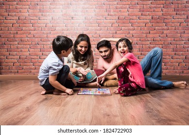 Indian Young Family Of Four Playing Board Games Like Chess, Ludo Or Snack And Ladder At Home In Quarantine