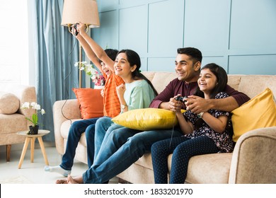 Indian young family of four playing video game using controller or joystick while sitting on sofa